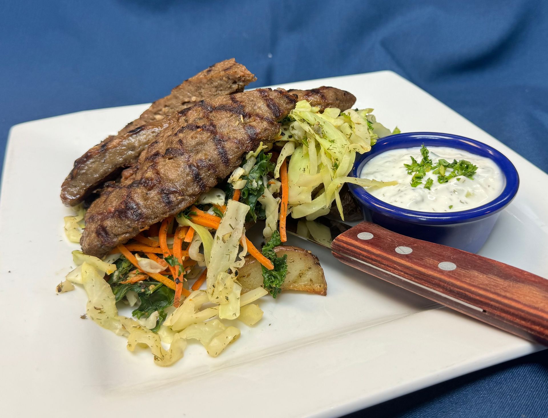 A white plate topped with meat , vegetables and a dipping sauce from Jake and Telly's
