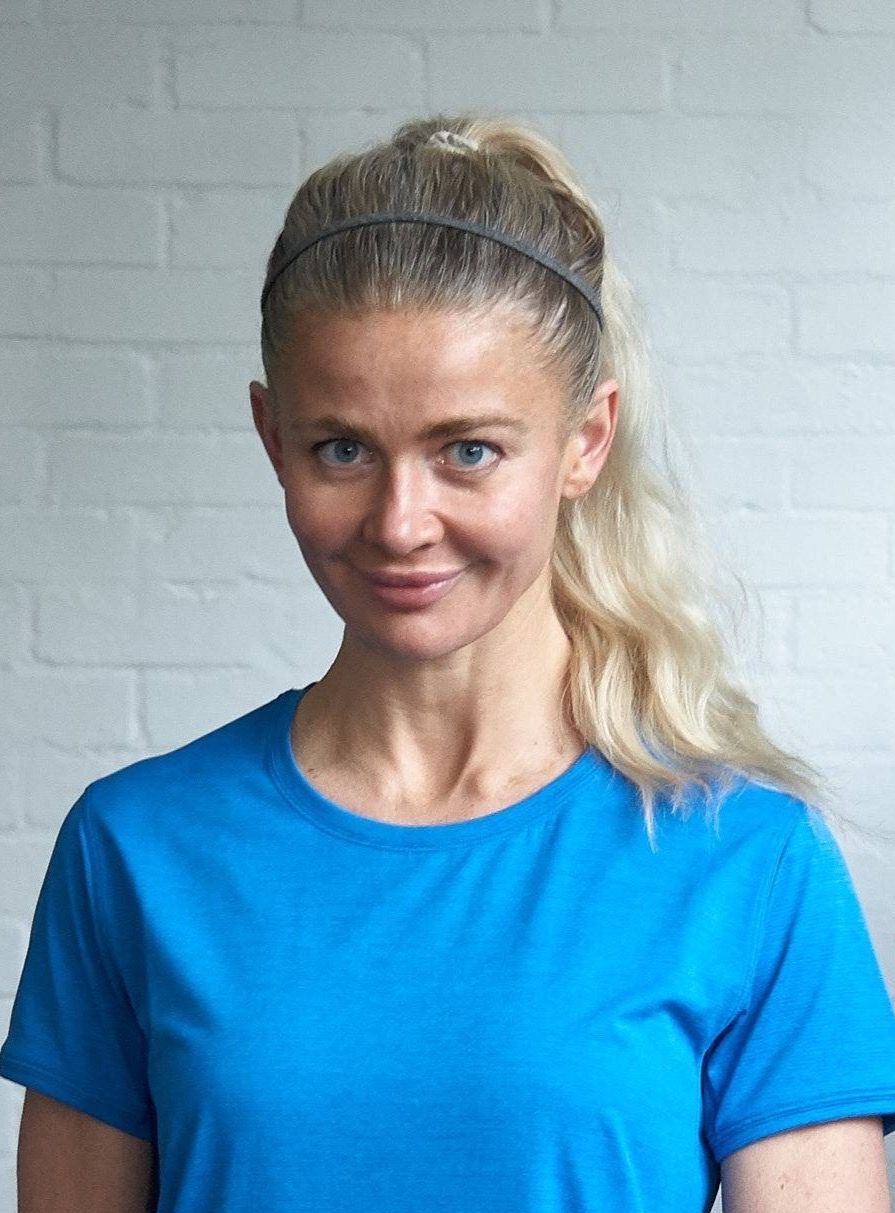 A woman wearing a blue shirt and a headband is standing in front of a white brick wall.