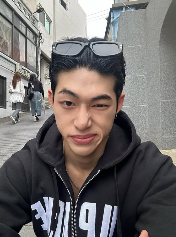 Woman wearing a surgical mask; dark hair; eyebrow makeup and eyeliner visible.