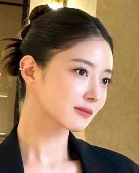 Woman with dark hair in a bun, wearing a ear cuff, and a black jacket, looking to the side.