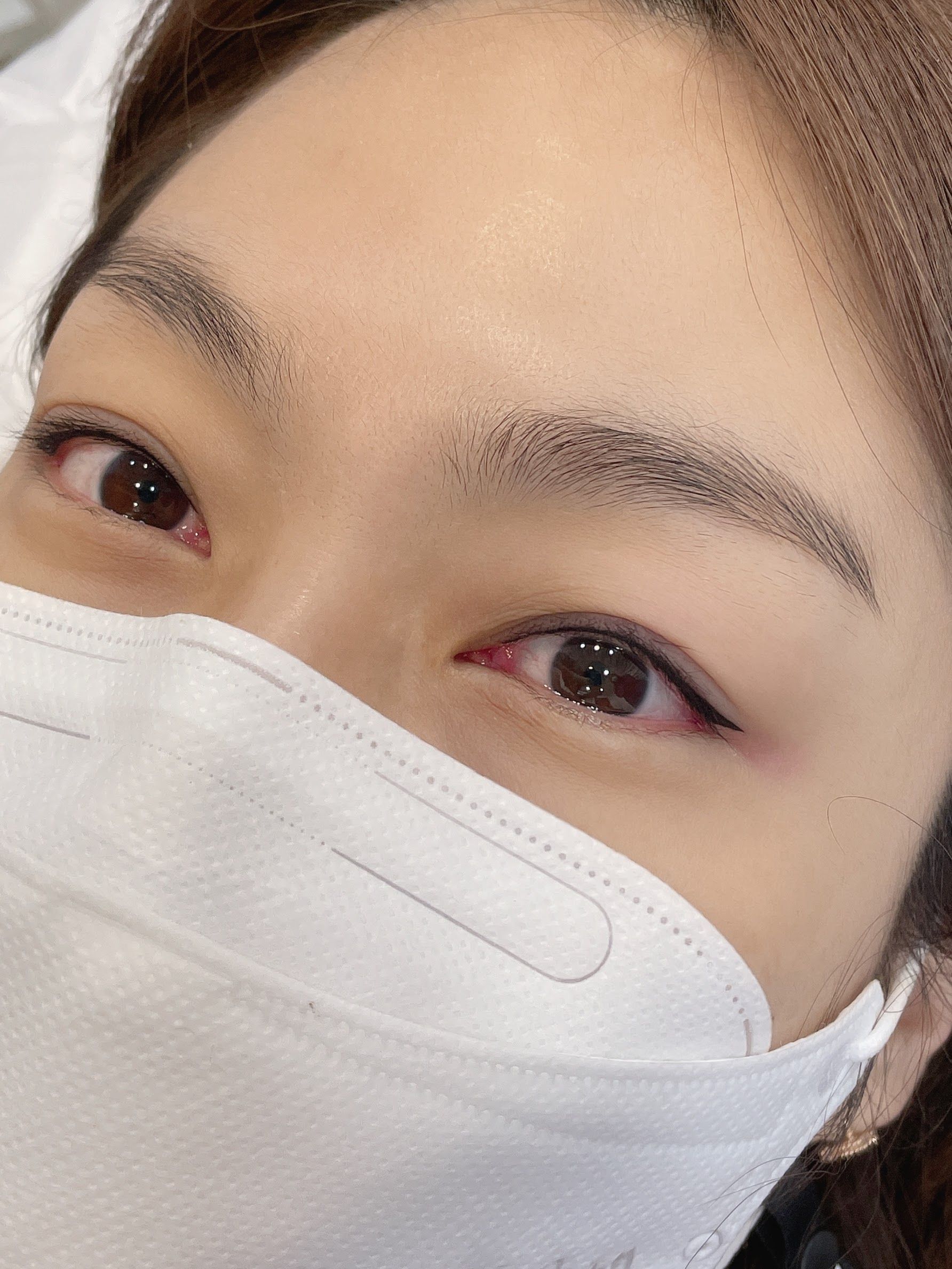 Close-up of eyes and eyebrows, partially obscured by a white mask. Black eyeliner and light eyebrows are visible.