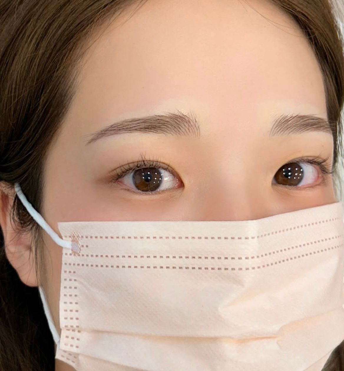Close-up of person's eyes, eyebrows, and mask. Light brown eyes, light skin, peach-colored mask.