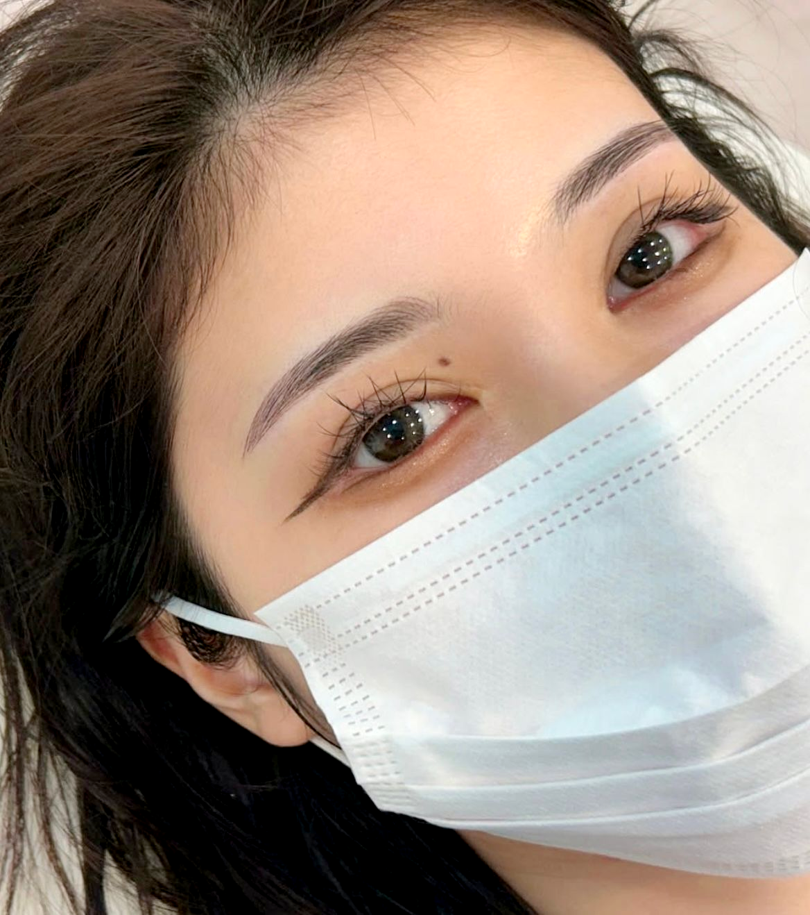 Woman with a face mask, light skin, short brown hair, looking at the camera.