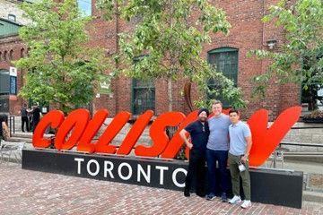 three men are posing for a picture in front of a toronto sign .