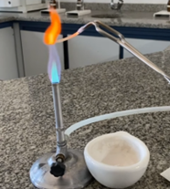 A flame test experiment showing a glowing orange flame produced by a wire being held over a Bunsen burner in a lab.