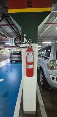A red fire extinguisher is mounted on a white, green, and red concrete pillar labeled 