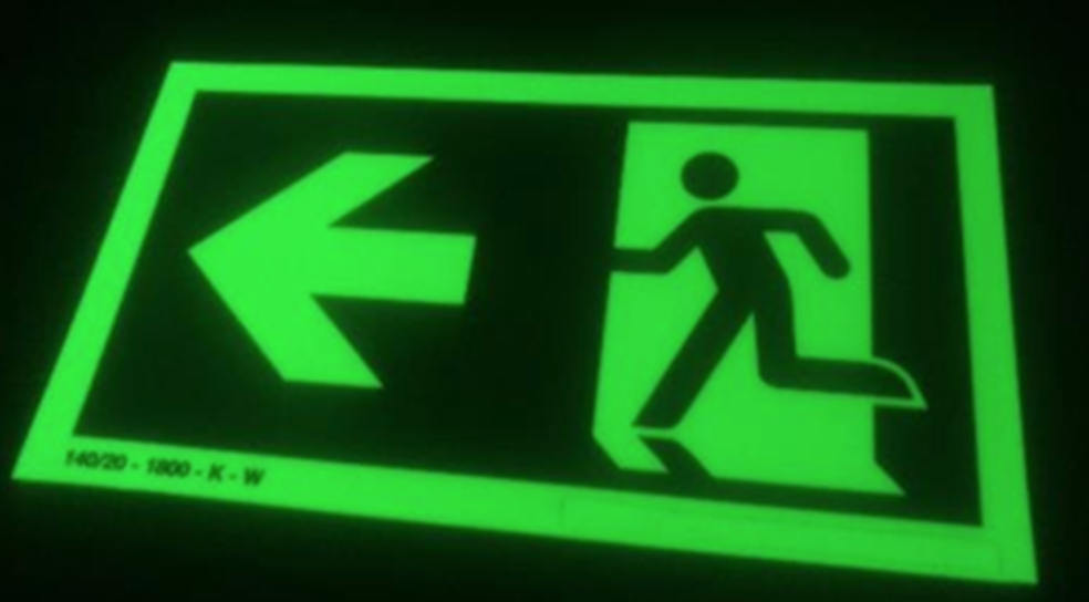 A glowing green emergency exit sign featuring a running person icon pointing toward a left-facing arrow.