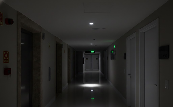 A dim, empty hotel-style hallway with doors on both sides, leading to a distant exit sign.