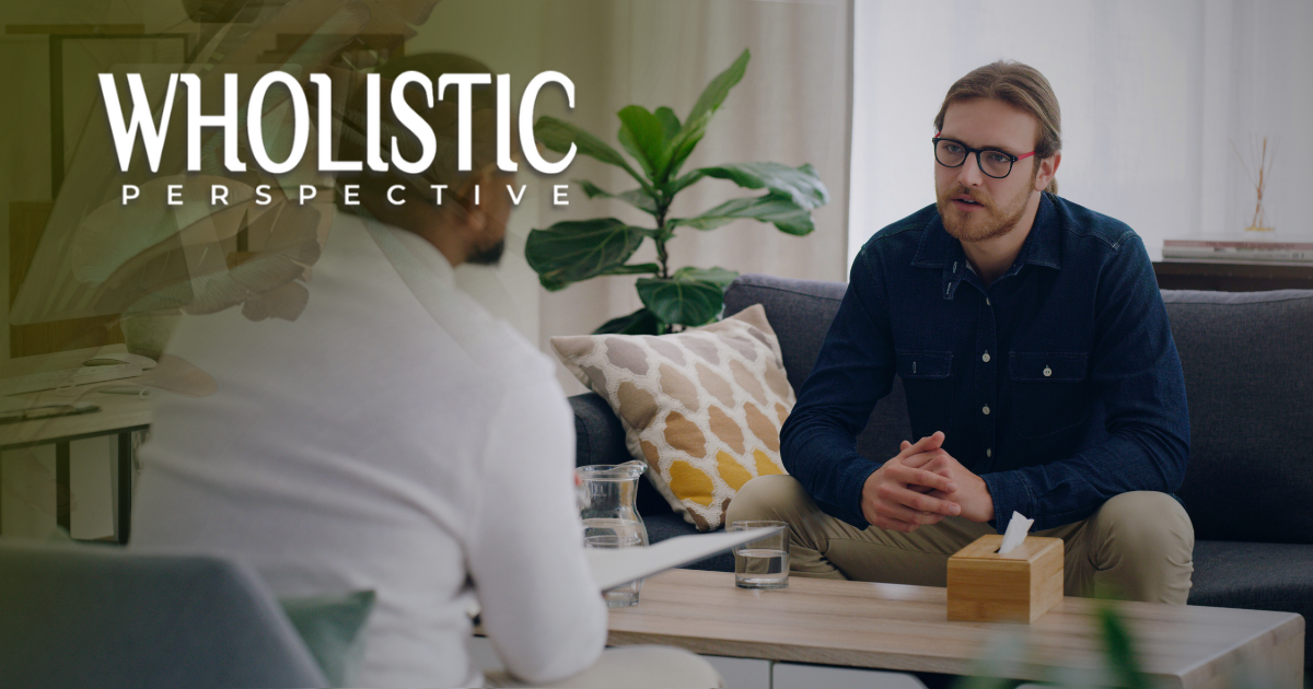 Two people sit in a living room during an interview, with the text 