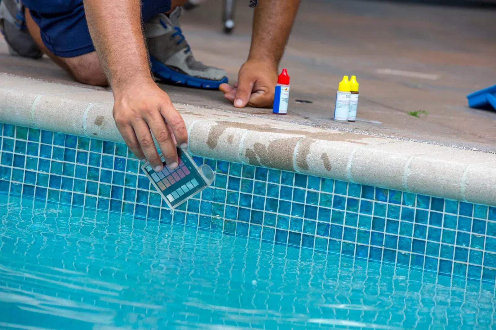 A man is taking a sample of water from a swimming pool.