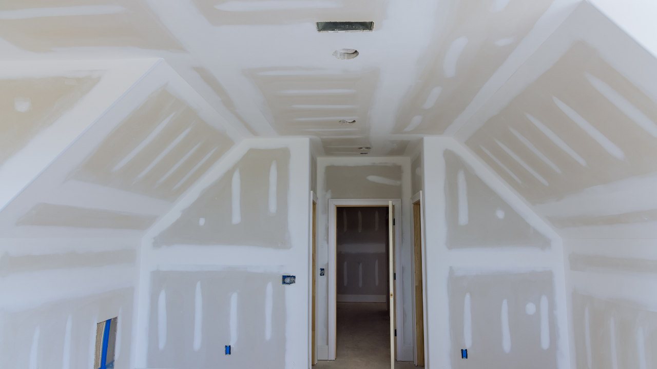 Interior of a newly constructed room with drywall installed. White walls and ceiling, hallway in background.