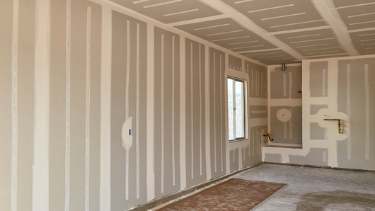 Interior of a room with drywall installed on walls and ceiling, ready for finishing.