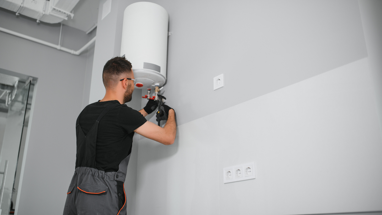 Plumber installing a white water heater on a gray wall.