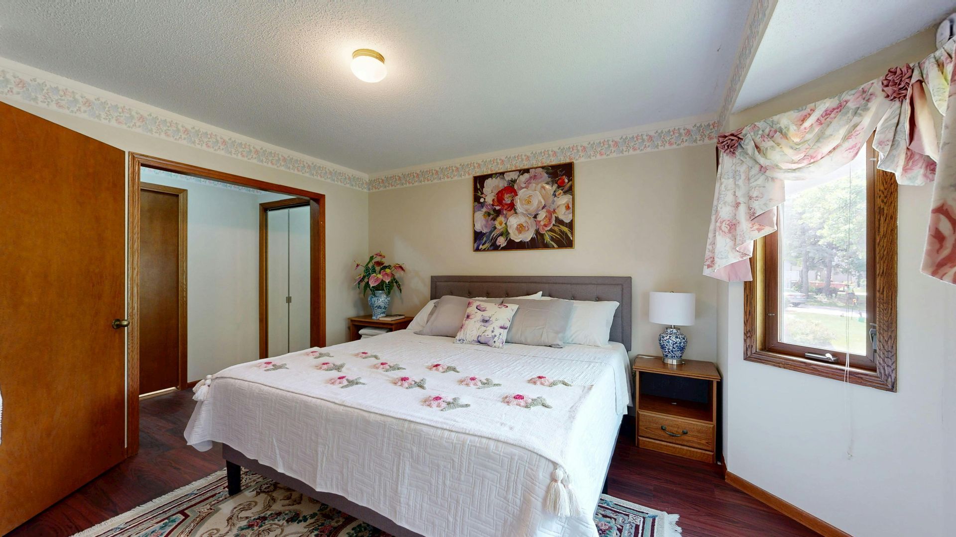 Bedroom with a bed, nightstand, window with curtains, and artwork on the wall.