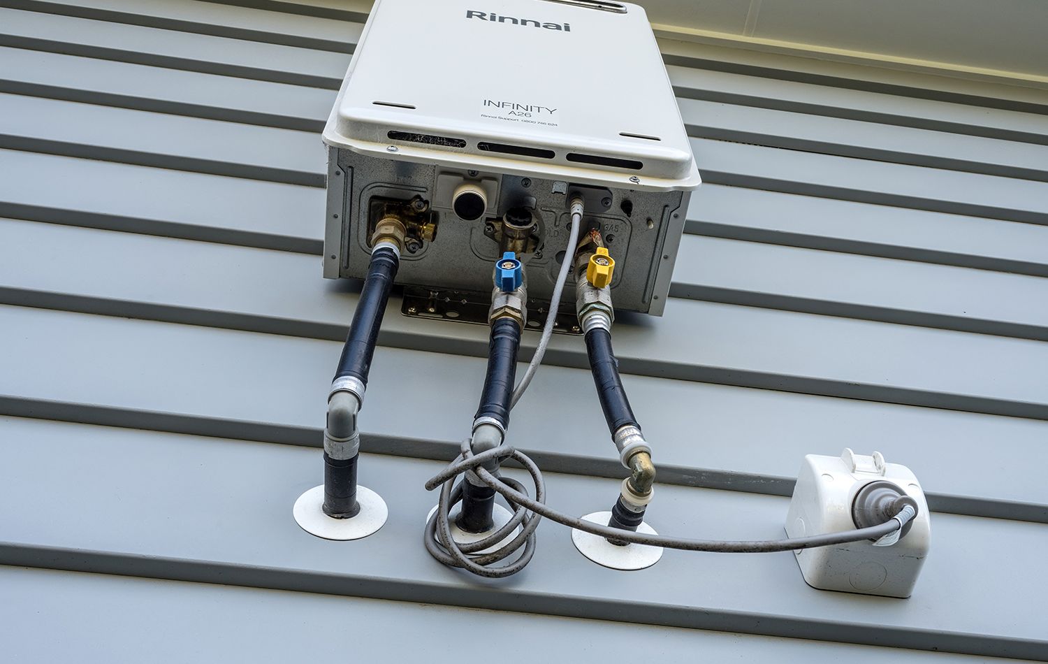 A plumber in work clothes kneeling in a bathroom, using a wrench to tighten the pipe underneath a wall-mounted sink.