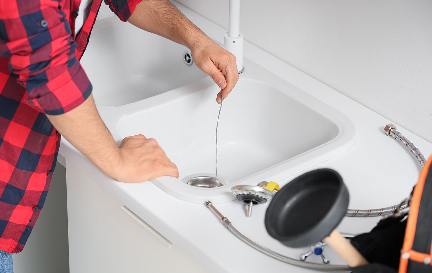 A plumber in work clothes kneeling in a bathroom, using a wrench to tighten the pipe underneath a wall-mounted sink.