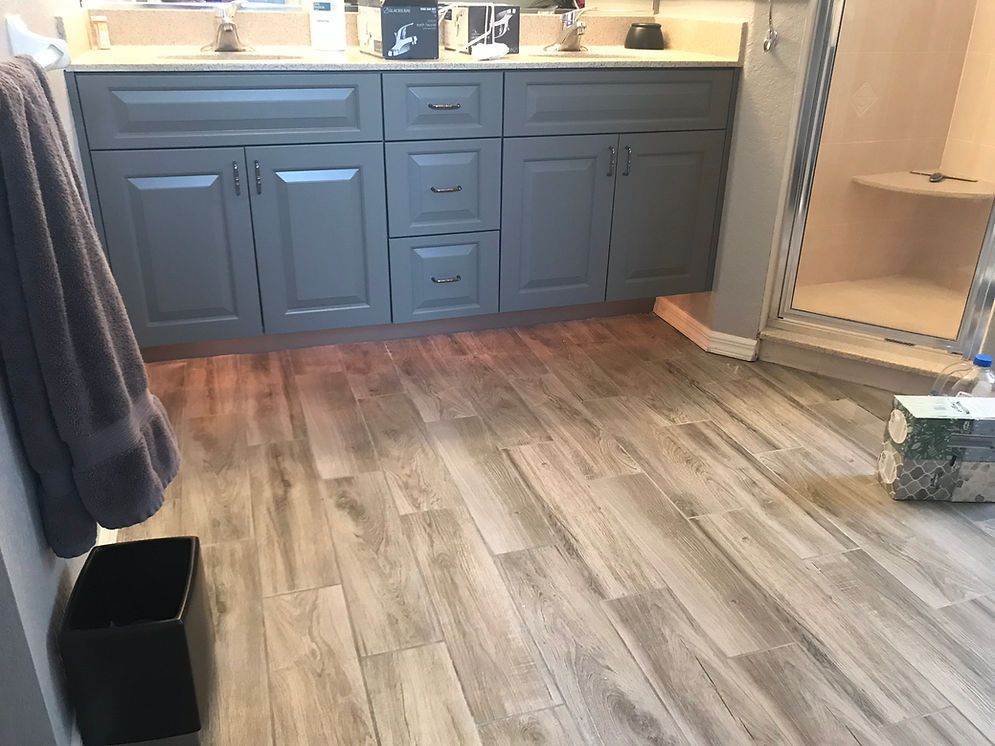 A bathroom with a wooden floor and gray cabinets.