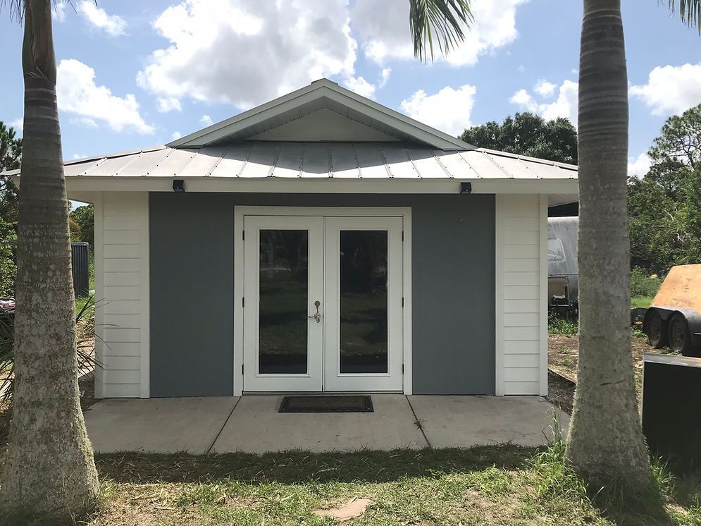 A small house with a metal roof is surrounded by palm trees.