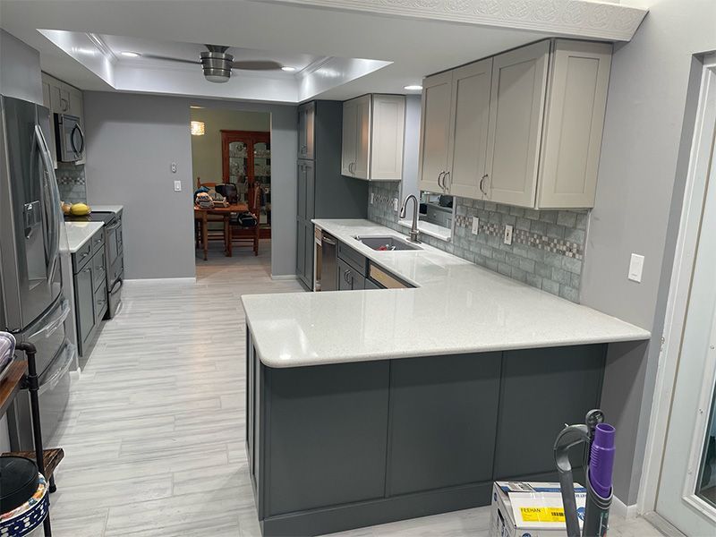 Modern kitchen with gray and white cabinets, white countertops, and blue tiled backsplash.