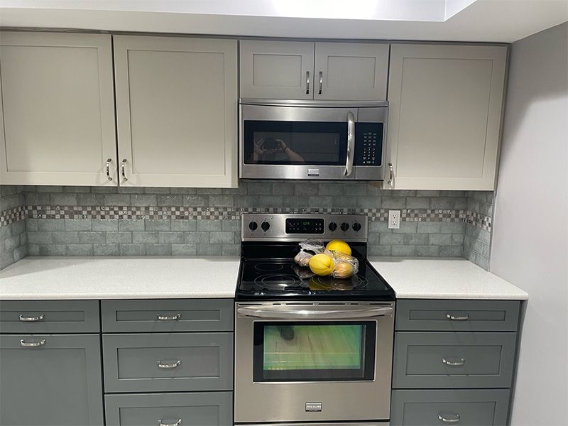 Kitchen with gray and white cabinets, stainless steel appliances, and mosaic backsplash.
