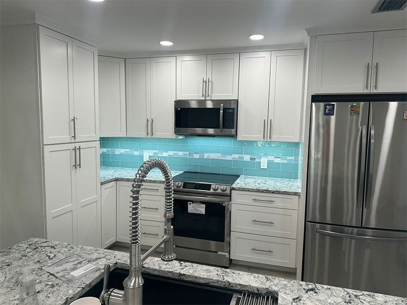 Modern white kitchen with turquoise backsplash, stainless steel appliances, and a granite countertop.