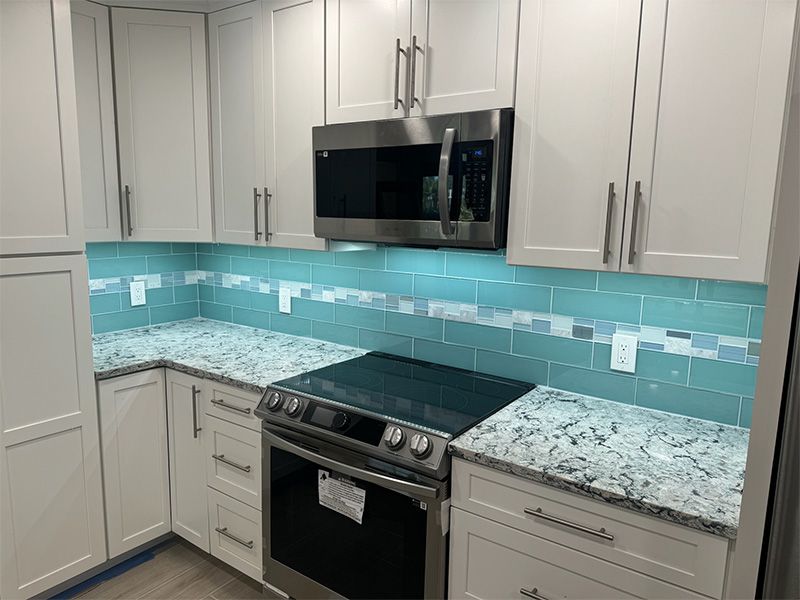 Modern kitchen with white cabinets, blue backsplash, and stainless steel appliances.