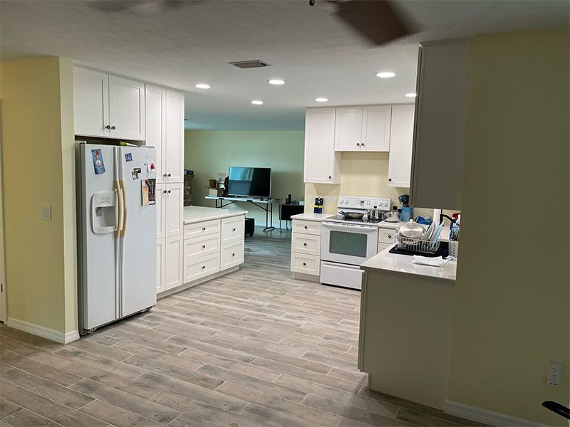 Bright kitchen with white cabinets, appliances, and tiled floor. Refrigerator on the left, stove on the right.