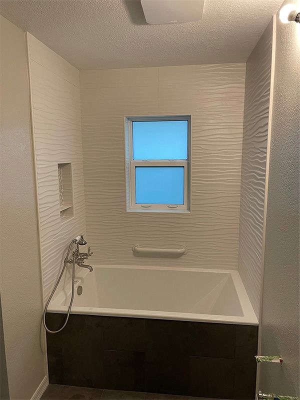 Bathroom with white tub, textured wall, window, and dark brown paneling.