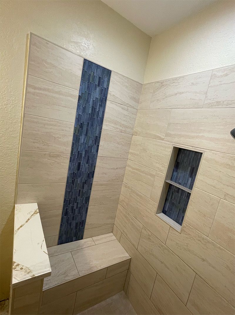 Shower stall with beige tile, a blue accent strip, and a built-in bench.
