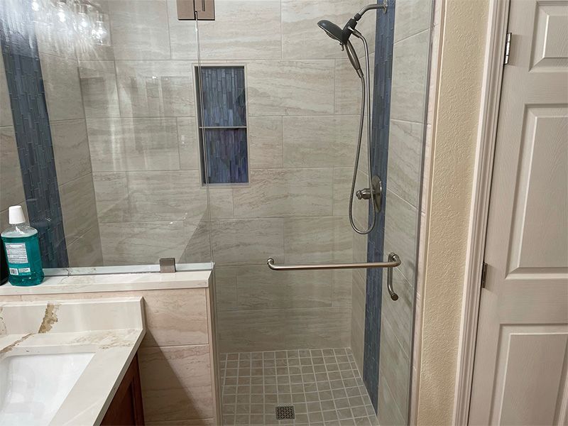 Modern bathroom with a glass shower, light tile, and a chrome grab bar.