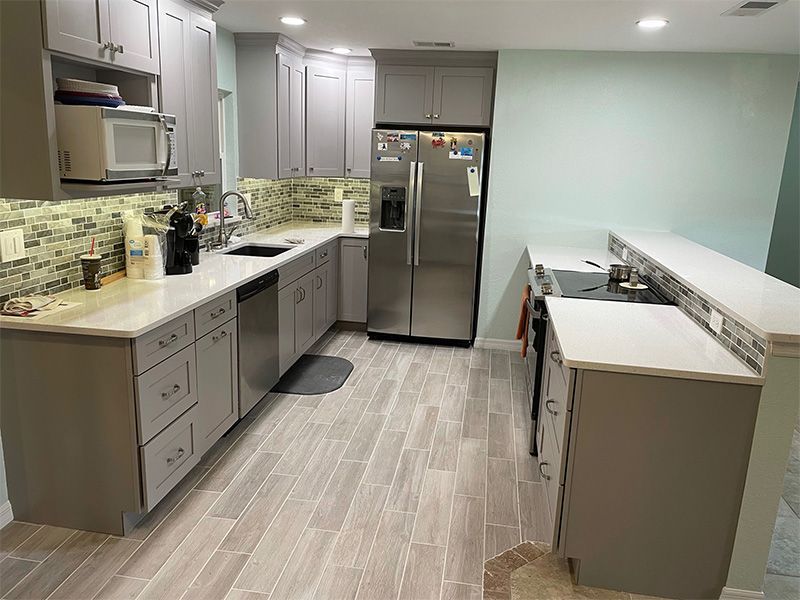 Gray kitchen with light wood-look flooring, stainless steel appliances, gray cabinets, and light-colored countertops.