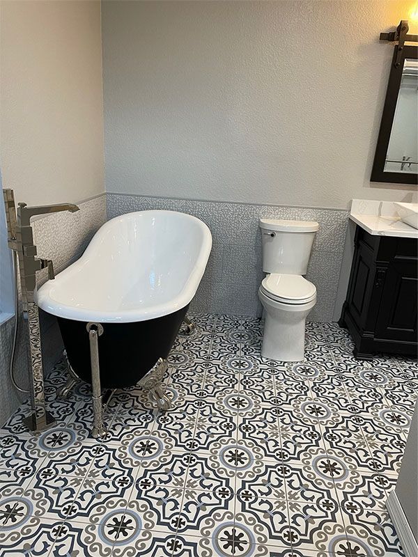 Bathroom with black clawfoot tub, patterned floor tiles, toilet, and dark vanity.