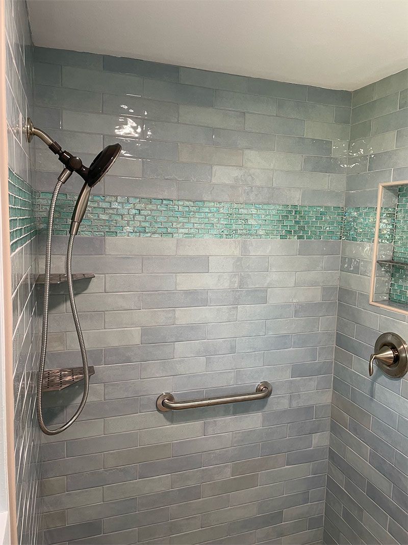 Shower with light blue textured tiles, a green glass tile stripe, and a grab bar.