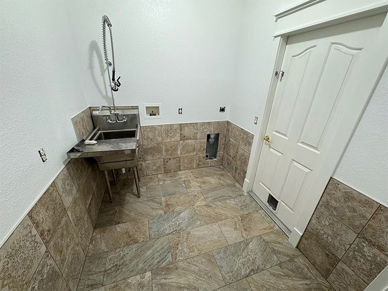 Laundry room with stainless steel sink, tile flooring, and white walls. Door on the right.