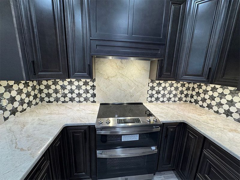 Kitchen with black cabinets, stainless steel stove, star-patterned backsplash, and light countertops.