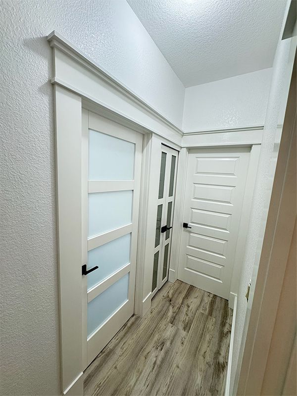 A hallway with white doors of different styles, black handles, and light wood-look flooring.