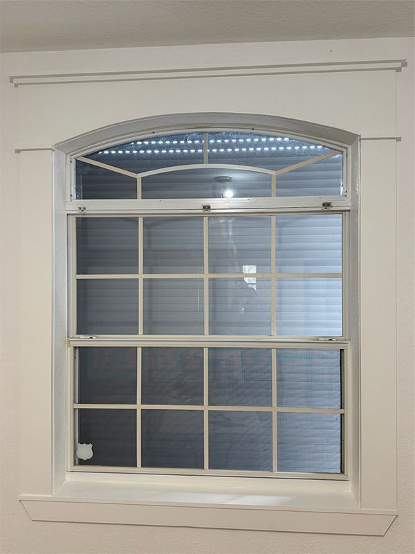 White framed window with arched top and grid panes, mounted in a white wall with decorative trim.