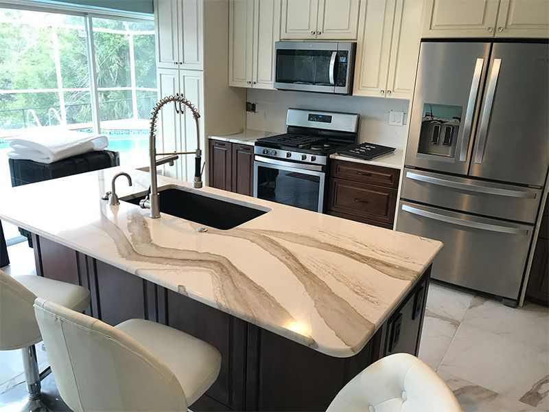 Modern kitchen with island, stainless steel appliances, light countertops, dark cabinets, and pool view.