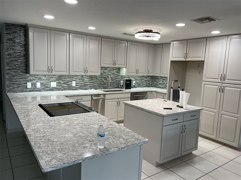 A modern kitchen with light gray cabinets, granite countertops, and a central island.