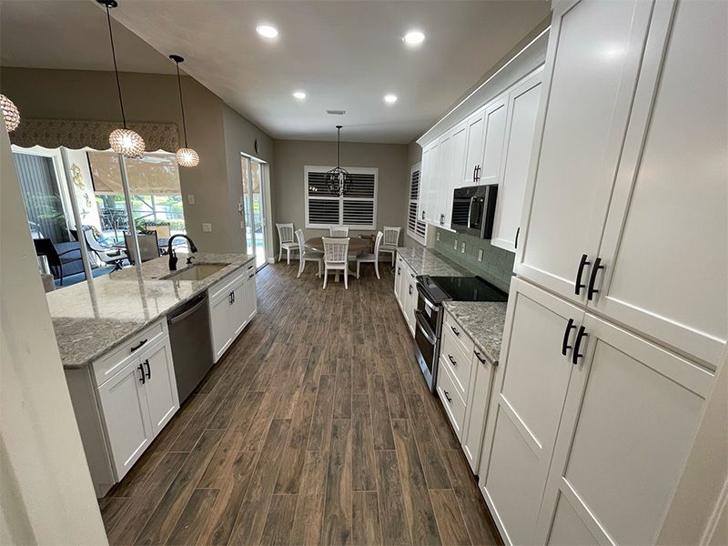 Modern kitchen with white cabinets, stainless steel appliances, and wooden floors.