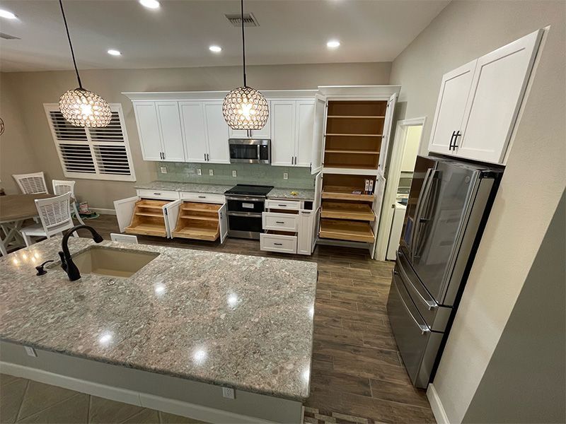 Kitchen with white cabinets, granite countertop, stainless steel appliances, and brown wooden floor.
