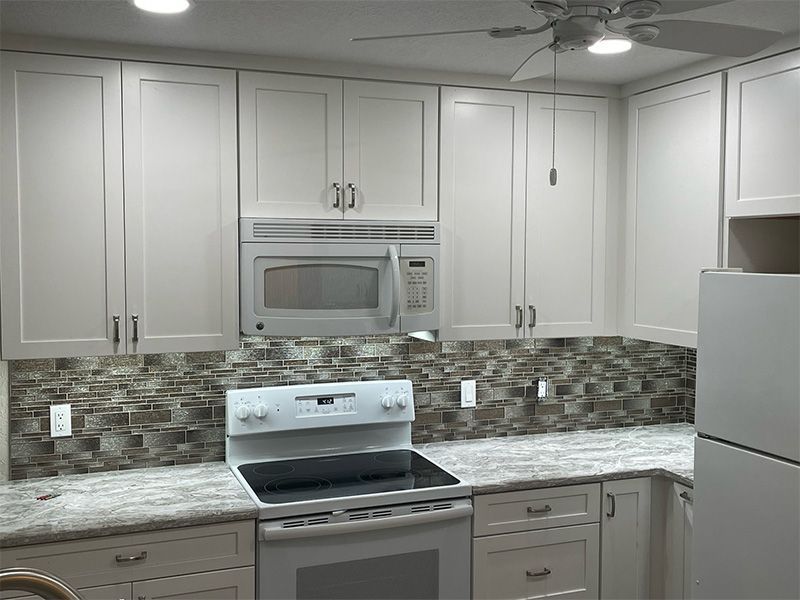 White kitchen with microwave above the stove. Neutral backsplash and granite countertops.