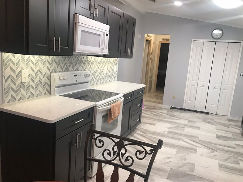 Kitchen with dark cabinets, white appliances, light countertops, herringbone backsplash, and gray flooring.