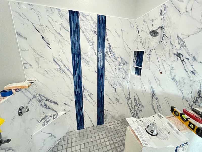 Shower with marble-like tile and blue mosaic accents. Tools and plans present, indicating construction.