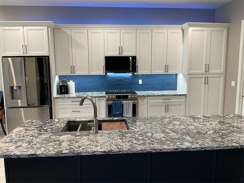 White kitchen with a blue backsplash, stainless steel appliances, and a granite island.