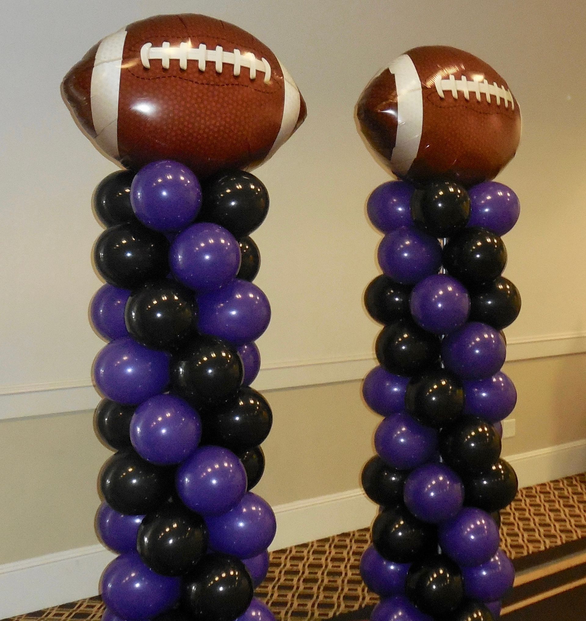 Two football shaped balloons are on top of purple and black balloons