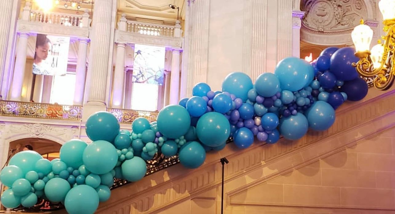 A bunch of blue balloons are hanging from the stairs of a building.