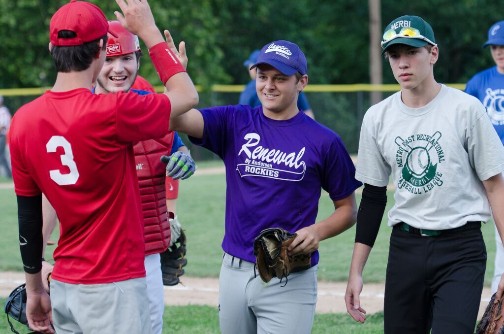 Baseball players high-fiving on a field, one in a purple 