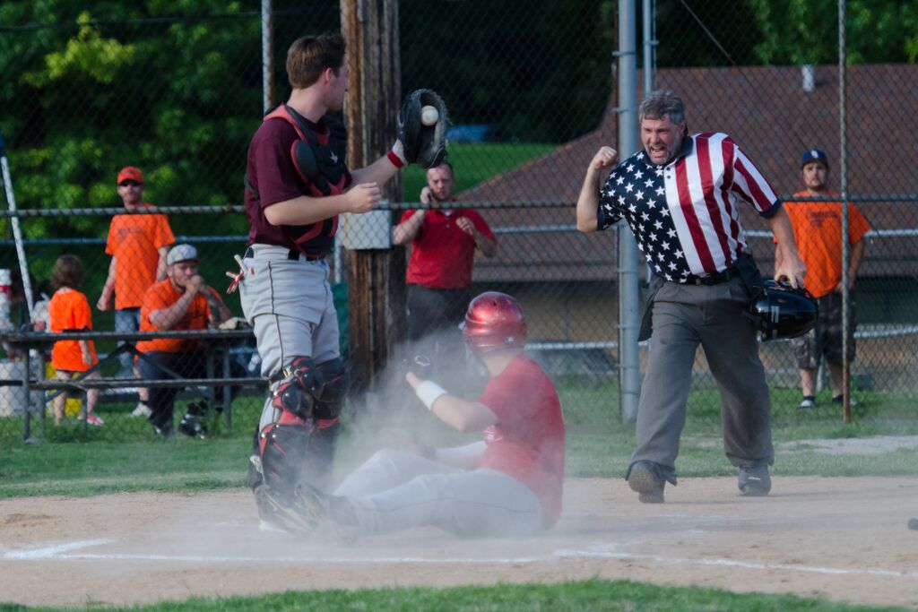 Baseball player sliding into home plate; umpire calls safe with a fist pump.