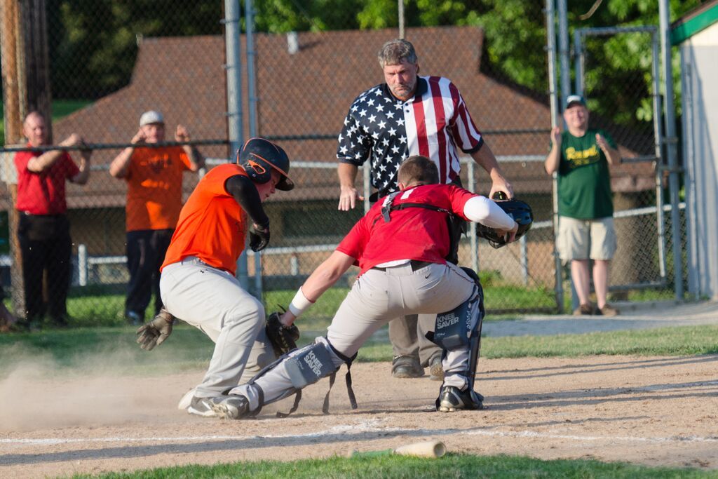 Baseball player sliding into home plate, umpire watching, others observing in background.